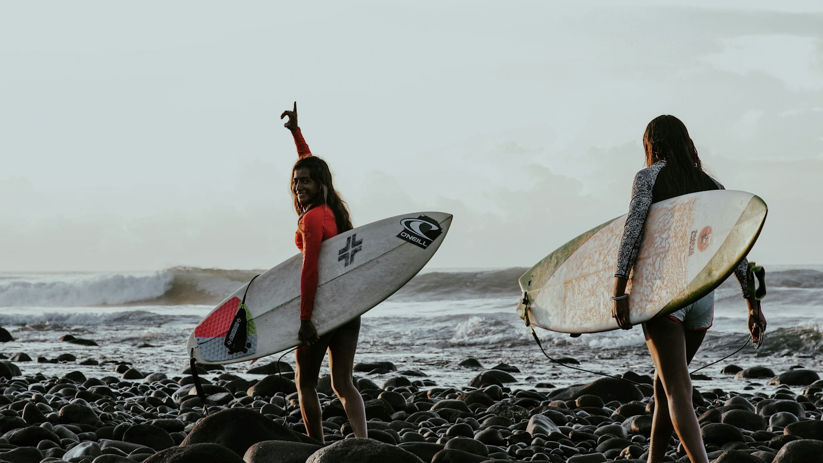 woman in red bikini holding white surfboard standing on rocky shore during daytime